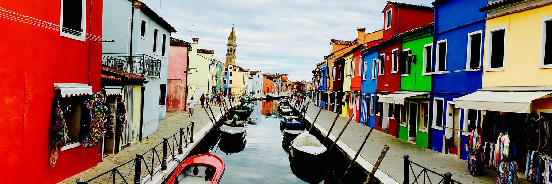 View of canals bordered by houses and boats docked to sides.