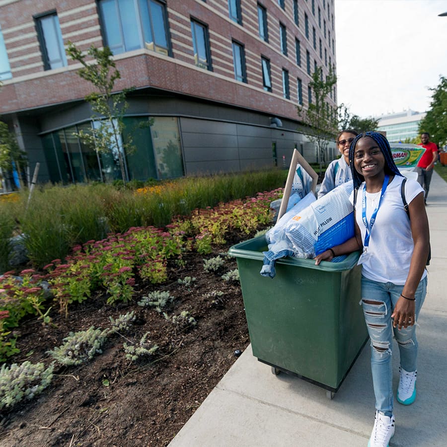 A student pulls a bin of things towards dorm on move in day.