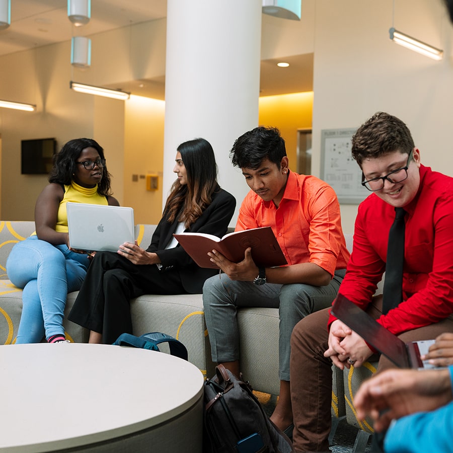 College of Management students informally sitting on couch reading a book, reviewing laptop and conferring