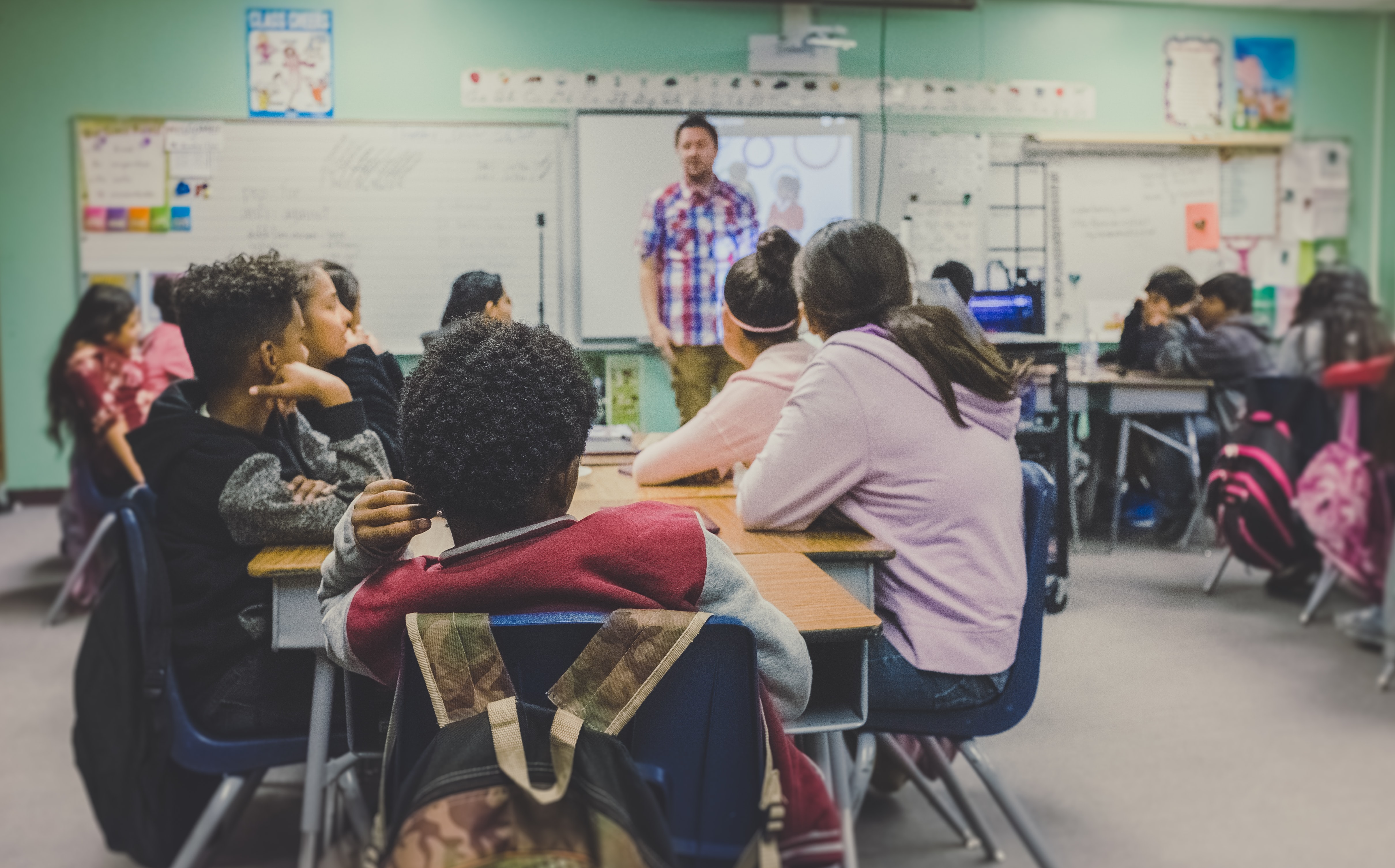 Students in a classroom listening to their teacher.  