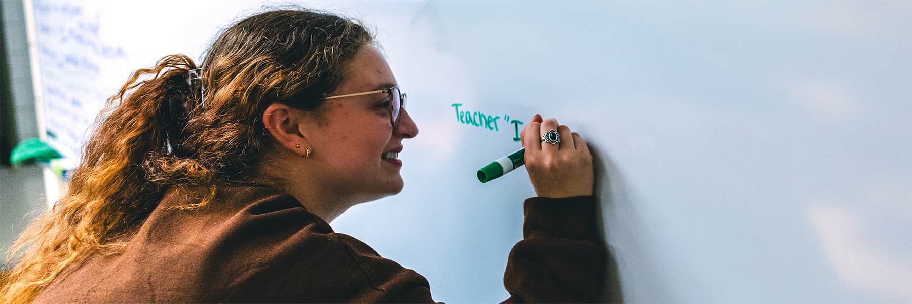 Teacher writing on whiteboard with green expo marker.