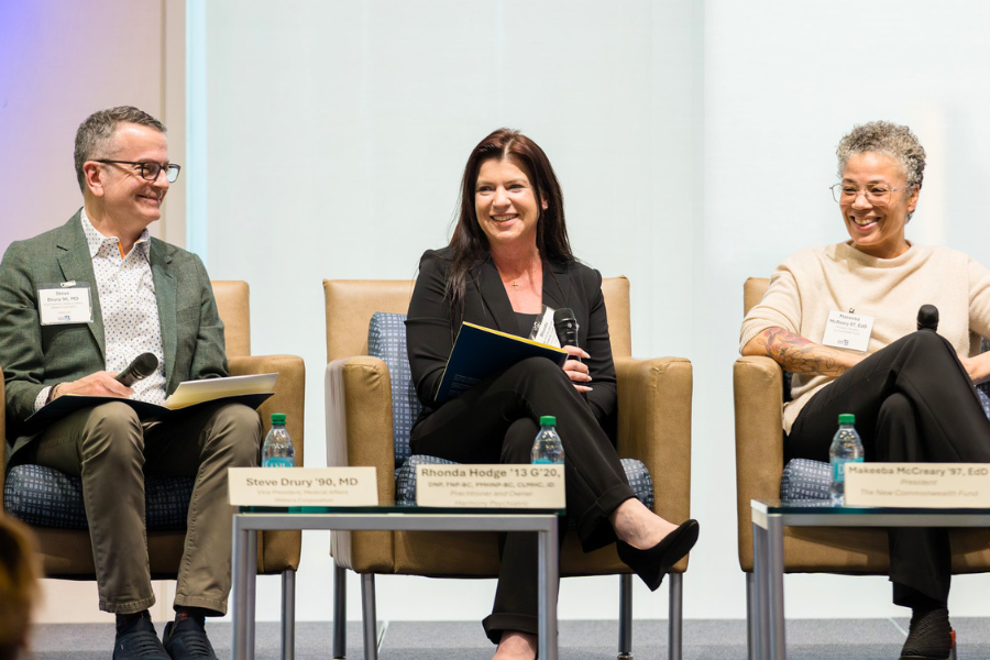 Three panelists seated onstage during a discussion event, smiling and holding microphones. Rhonda Hodge sits in the center between Steve Drury and Makeeba McCreary.