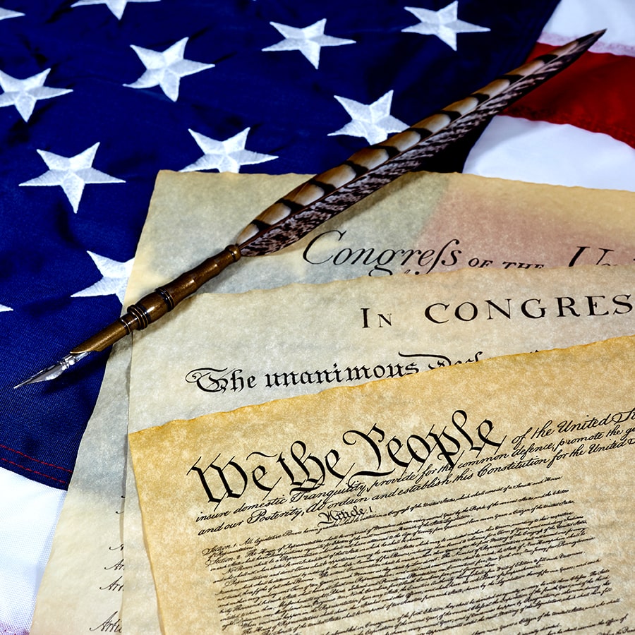 U.S. Constitution papers with pen and U.S. flag as backdrop