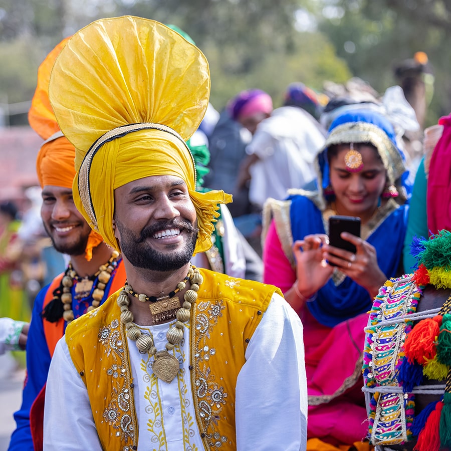 Bikaner, Rajasthan, India: Punjabi Bhangra, Portrait of young sikh male in traditional punjabi colorful dress and turban performing bhangra dance with smile in camel festival with selective focus.