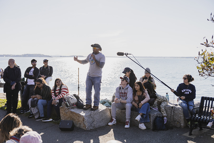 A group of people listening to a lecture with the Boston Harbor in the background.