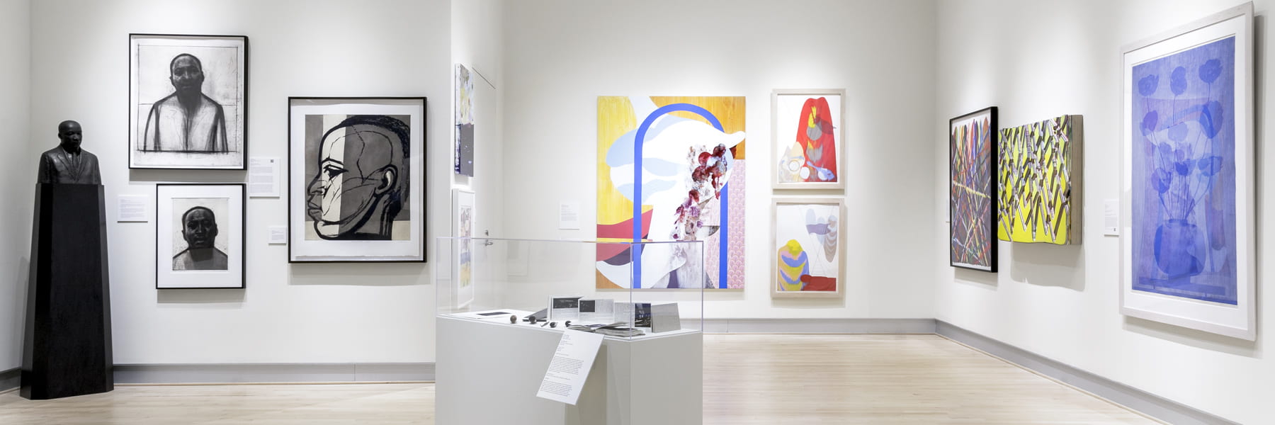 A wide shot of a bright, white art gallery filled with contemporary pieces.