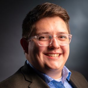 Man with short brown hair, glasses, blue shirt, brown blazer